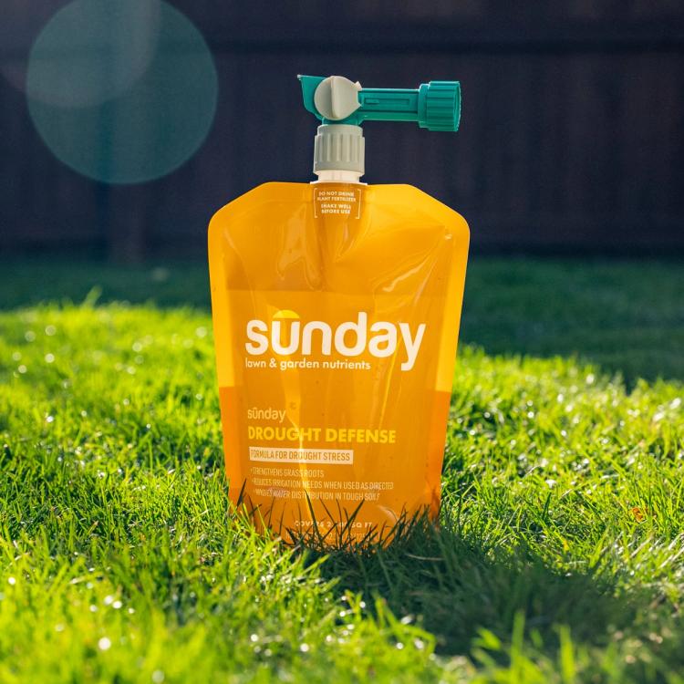 Drought Defense lawn fertilizer pouch sitting on green grass with sprayer attached.