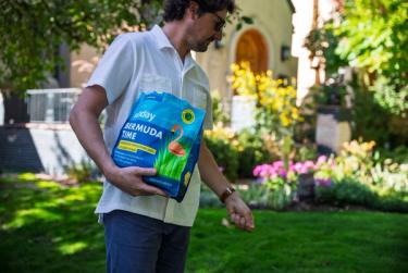 Man spreading Bermuda Time grass seed across lawn