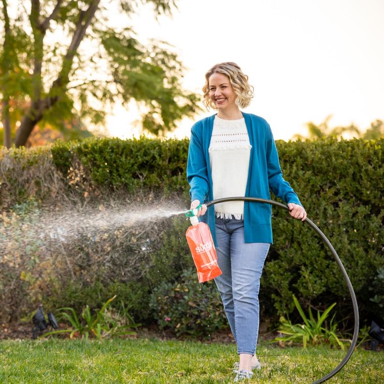 Woman spraying liquid lawn fertilizer on lawn