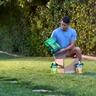 Person kneeling on a lawn beside an open Sunday lawn care box, holding a bag of lawn treatment with Sunday pouches set on the grass.
