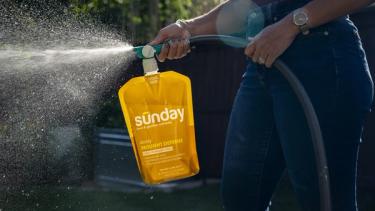 Person applying Sunday liquid lawn fertilizer products to lawn.