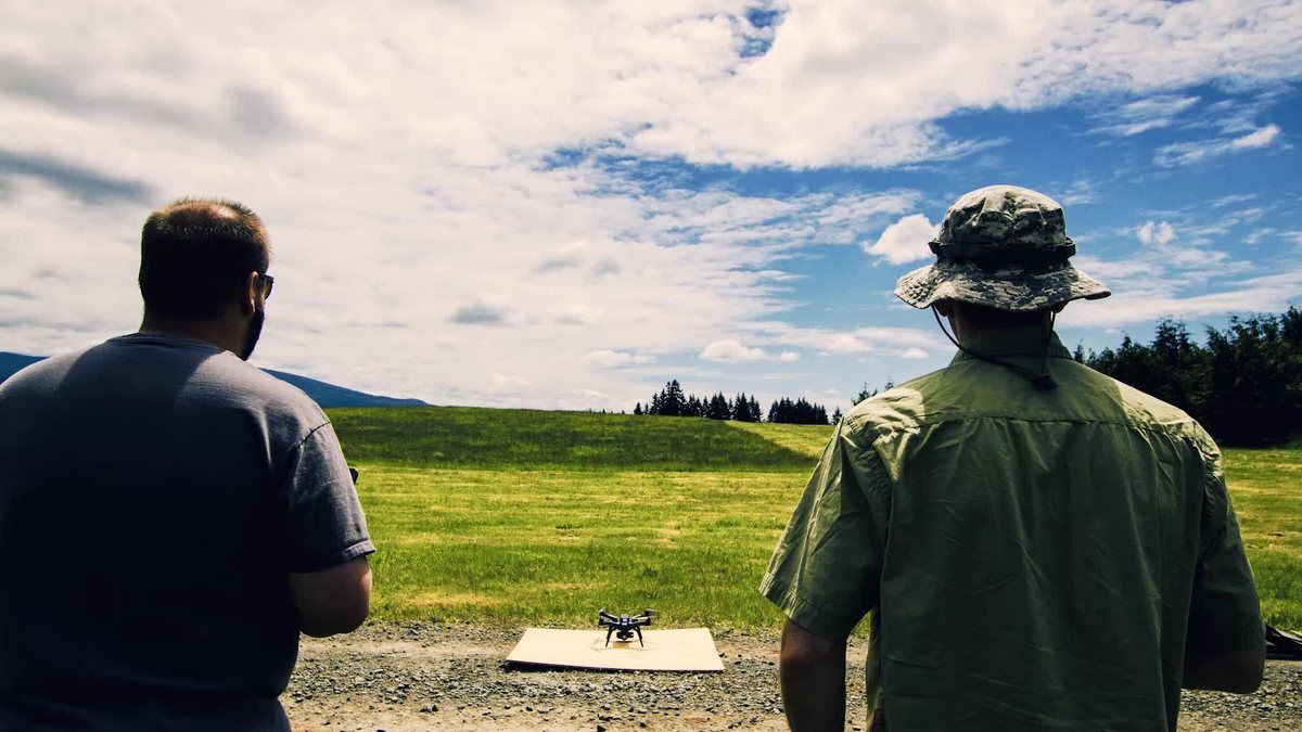Two people operating a small quadcopter drone in an open field.