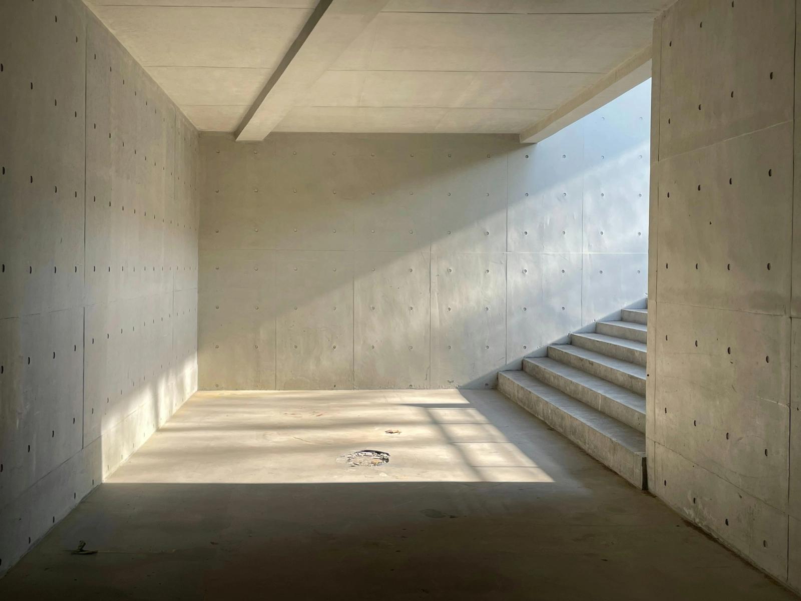 Cage d'escalier en béton brut et lisse, lumière du soleil qui arrive du haut des escaliers