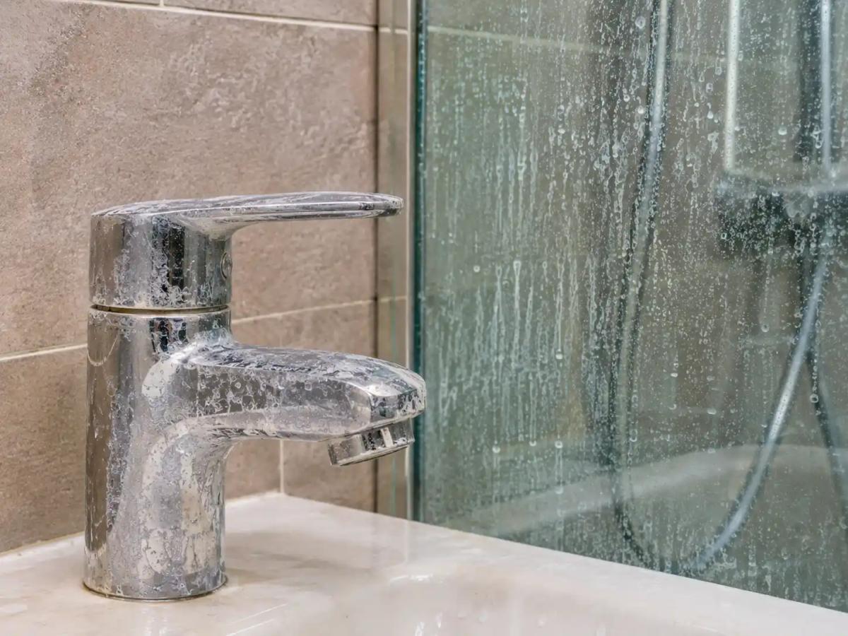 Hard water stains and limescale buildup on a bathroom chrome tap and glass shower screen