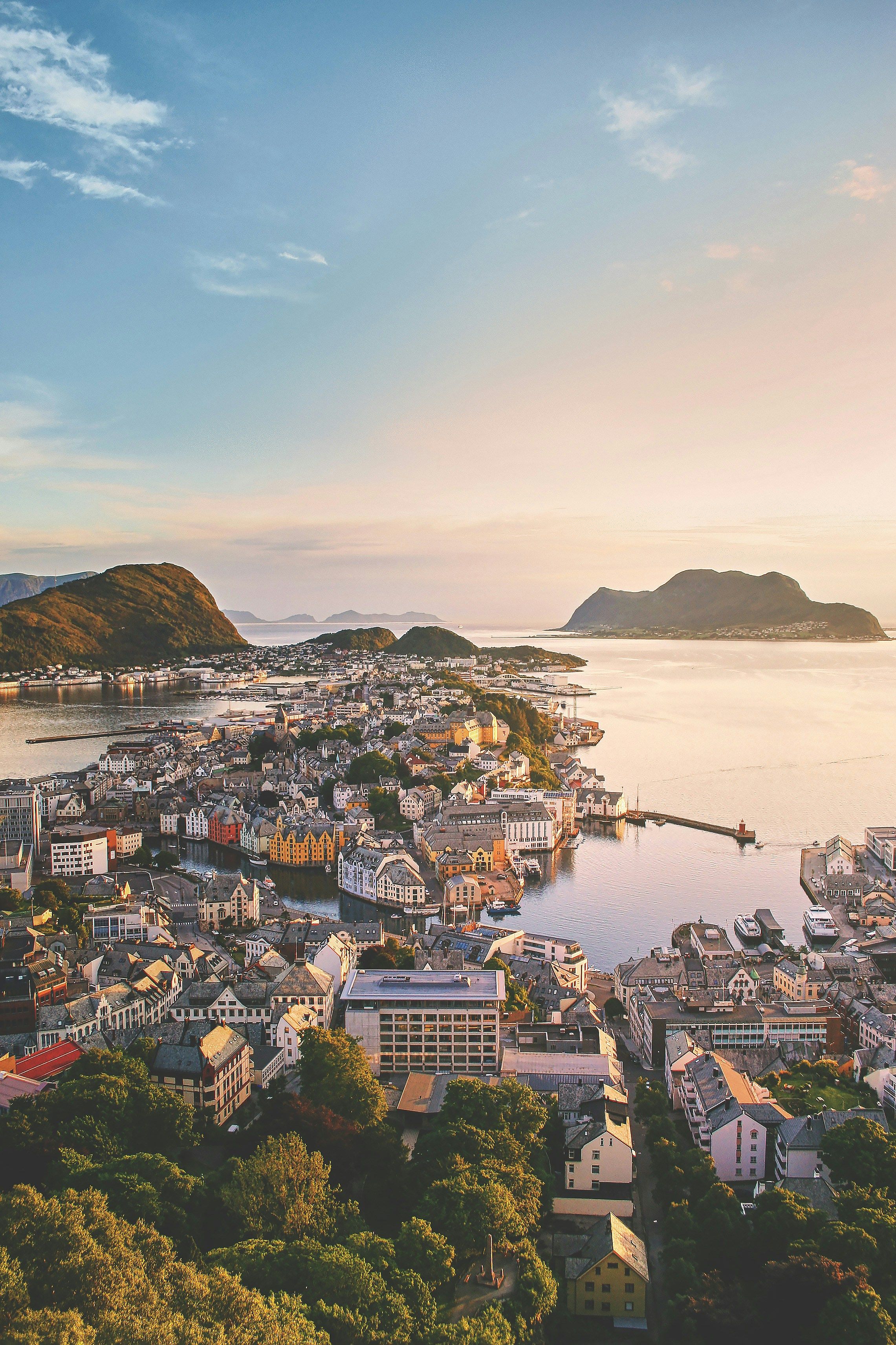 Utsikt over Ålesund sentrum i solnedgang, med jugendbebyggelse, sund og fjell i havet bakenfor.