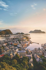 Utsikt over Ålesund sentrum i solnedgang, med jugendbebyggelse, sund og fjell i havet bakenfor.
