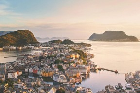Utsikt over Ålesund sentrum i solnedgang, med jugendbebyggelse, sund og fjell i havet bakenfor.