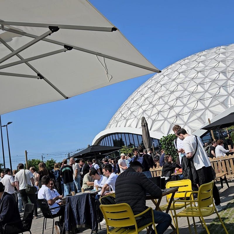 Konferanselokalet sett utvendig i sol, med masse mennesker rundt