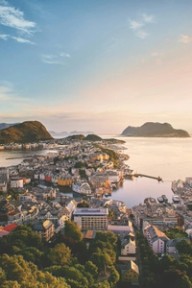 Utsikt over Ålesund sentrum i solnedgang, med jugendbebyggelse, sund og fjell i havet bakenfor.