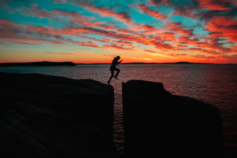 En person som hopper over et juv foran en fin solnedgang