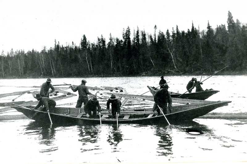 Two bateaux in river: three men in one, four men in the other, two men standing on logs. Allagash/St. John Rivers.