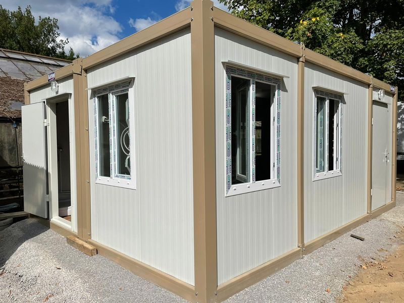 Newly delivered container guesthouse on gravel with protective film still on the window frames and the door open to a fitted shower room.