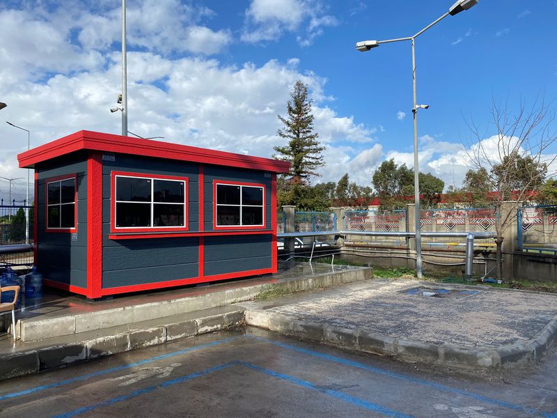 Dark grey Metro City site office with a bright red roof fascia and trim, raised on a kerb at an industrial entrance.