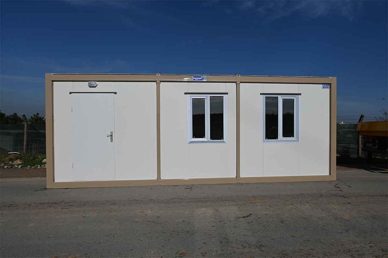White and beige standard container unit photographed square-on, with a personnel door and two windows.