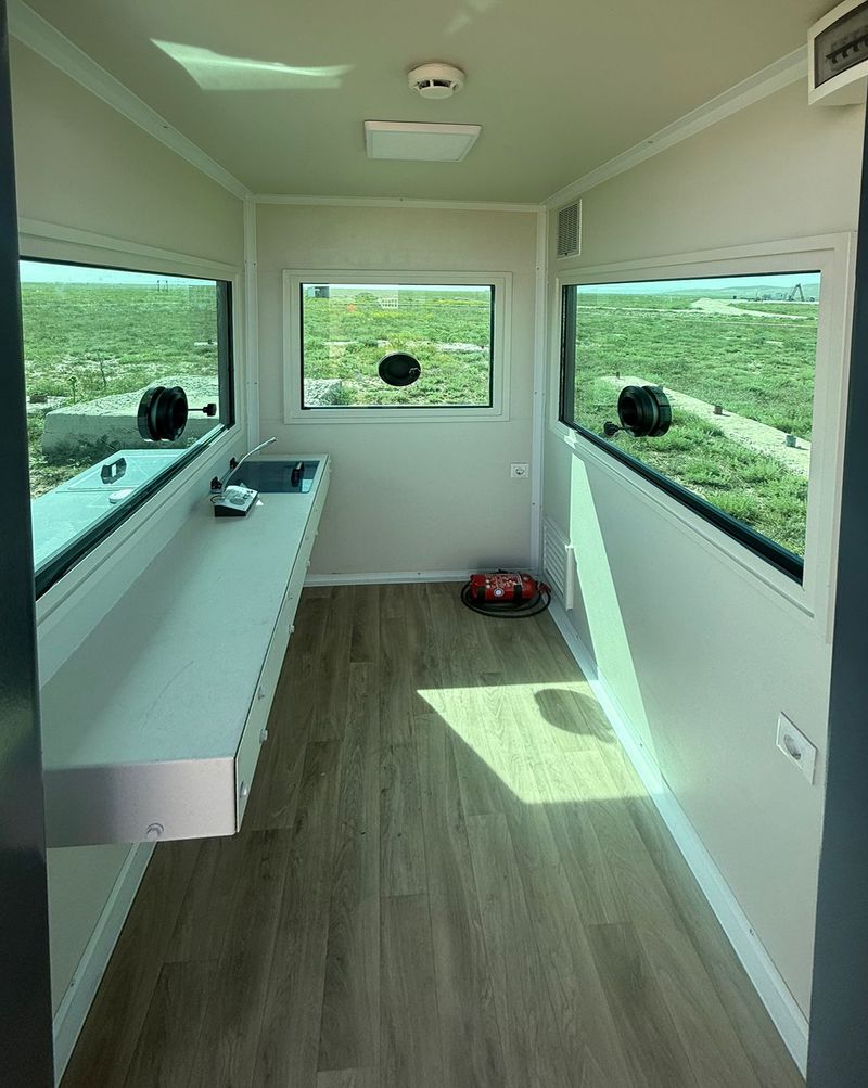 Interior of an armoured cabin, with a full-length worktop, wood-effect flooring and ballistic windows fitted with firing ports on three sides.