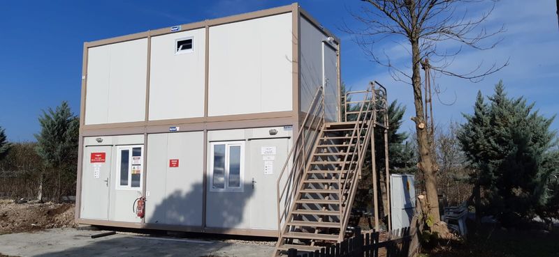 Two-storey white and beige container office block with an external steel staircase to the upper floor.