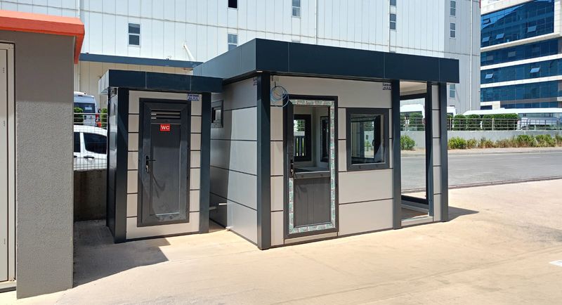 Grey Metro City cabin with a canopy and a separate WC cubicle alongside, at the entrance to an industrial site.