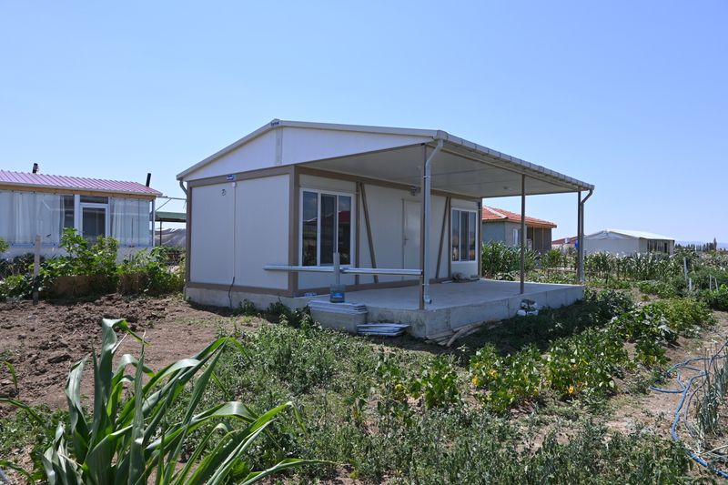 White container house with a deep canopy over a concrete terrace, standing in a vegetable garden near Ankara.