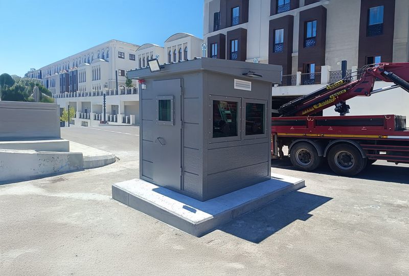 Grey armoured security cabin on a concrete plinth at a financial centre, with the delivery crane still alongside.
