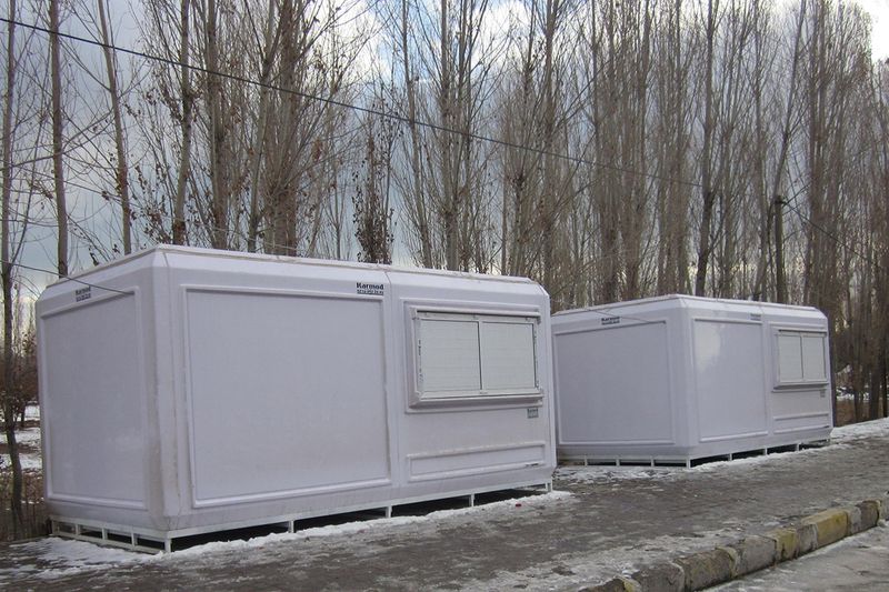 Two white GRP cabins standing in snow at a roadside, with bare poplar trees behind them.