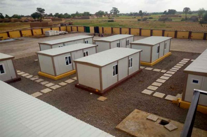 Elevated view of a container camp of single-storey units arranged around paved walkways inside a walled compound.
