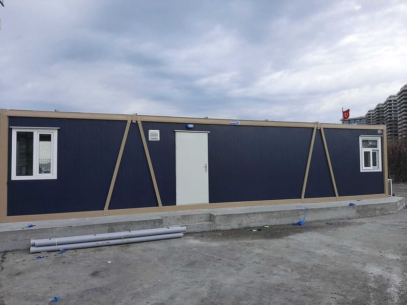 Long navy blue container office unit on a concrete plinth, with residential towers behind.