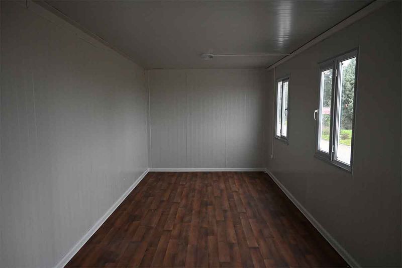 Empty interior of a standard container unit, with lined walls, wood-effect flooring and two windows.
