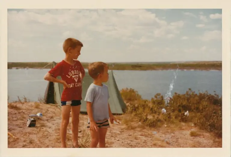 Two boys stand outside a tent at a campground beside a lake  