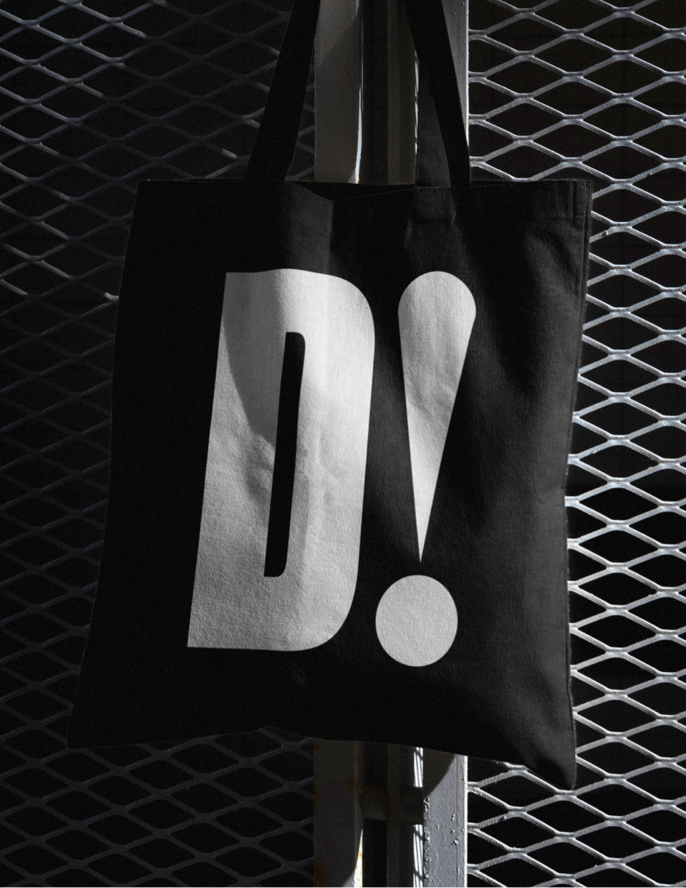 D! tote bag hanging on a metal fence