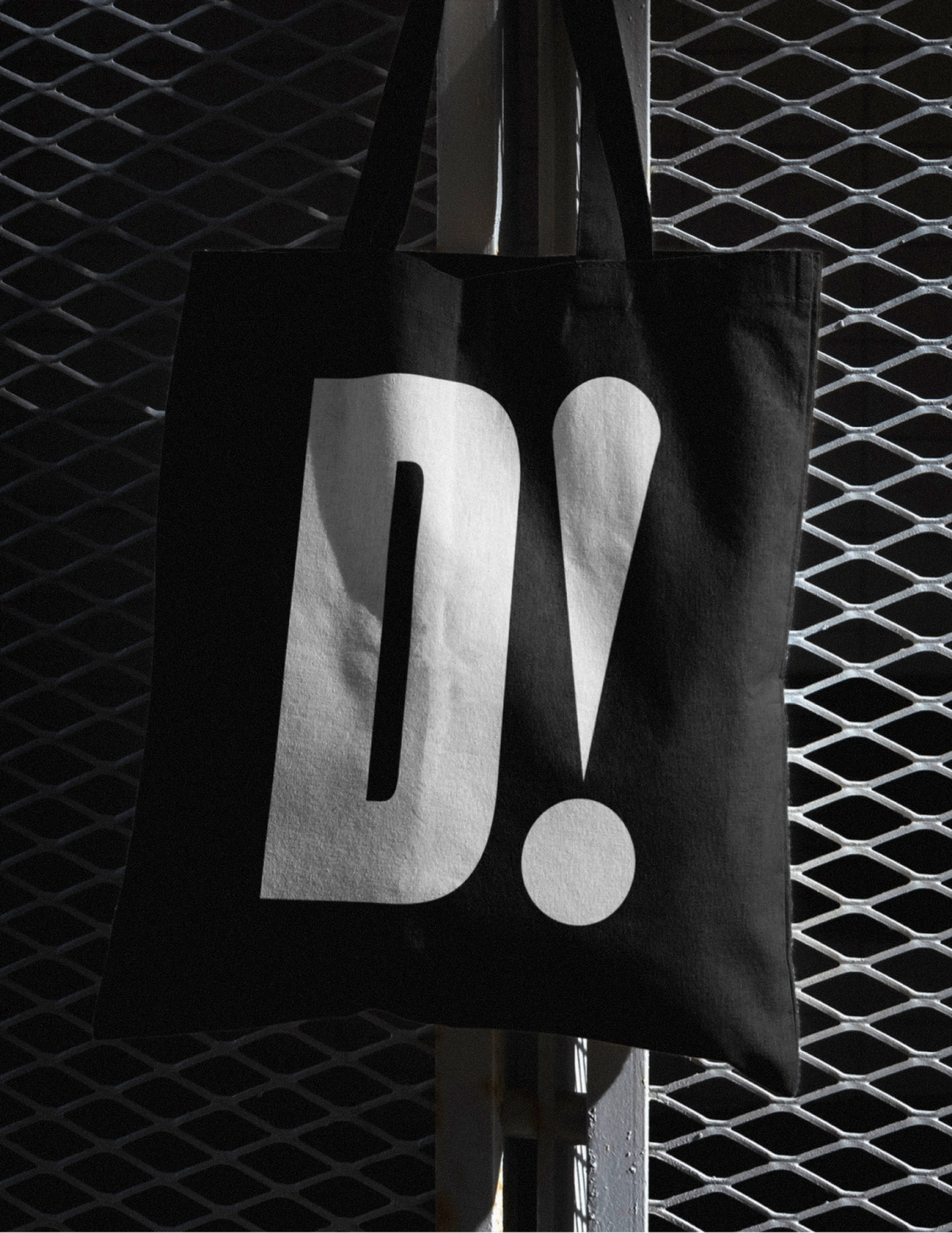 D! tote bag hanging on a metal fence