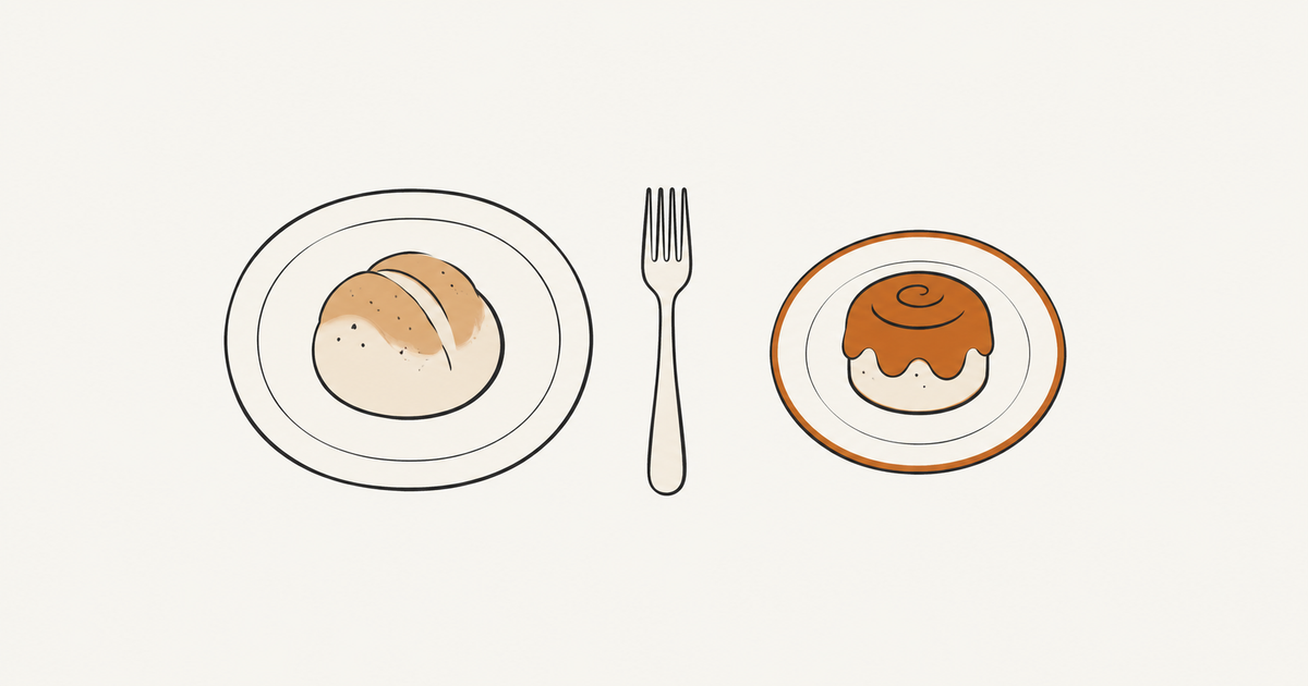 A bread roll and an iced pastry on separate plates, with a fork between them.