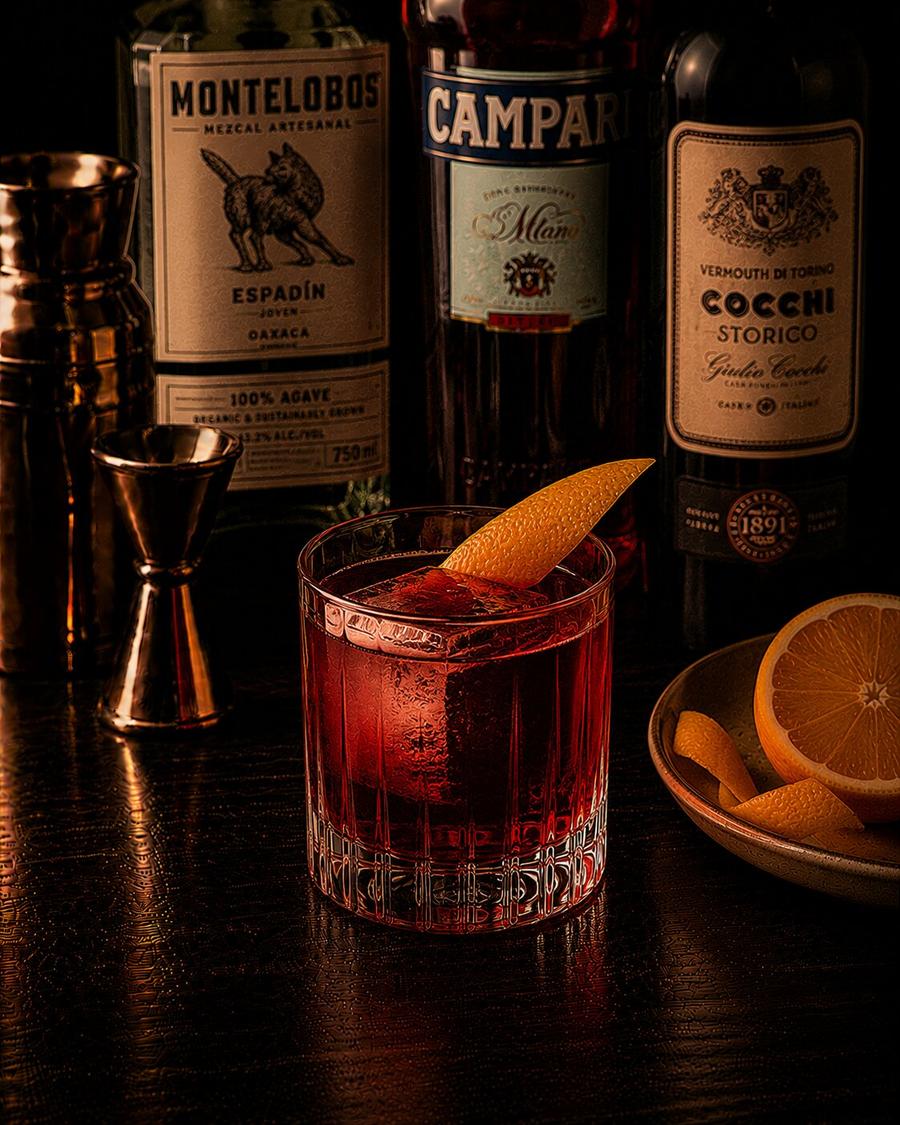 Mezcal Negroni drink with large ice cube and orange peel wedge