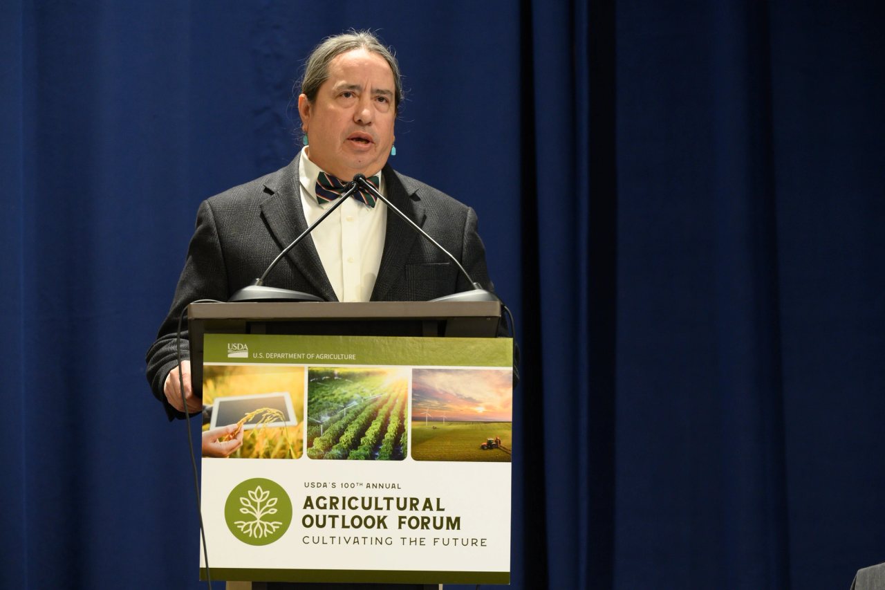 Michael Kotutwa Johnson speaking at a podium at the 2024 USDA Agricultural Outlook Forum.