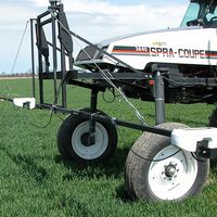 A field applicator fitted with light-reflectance sensors moves through a green crop field.