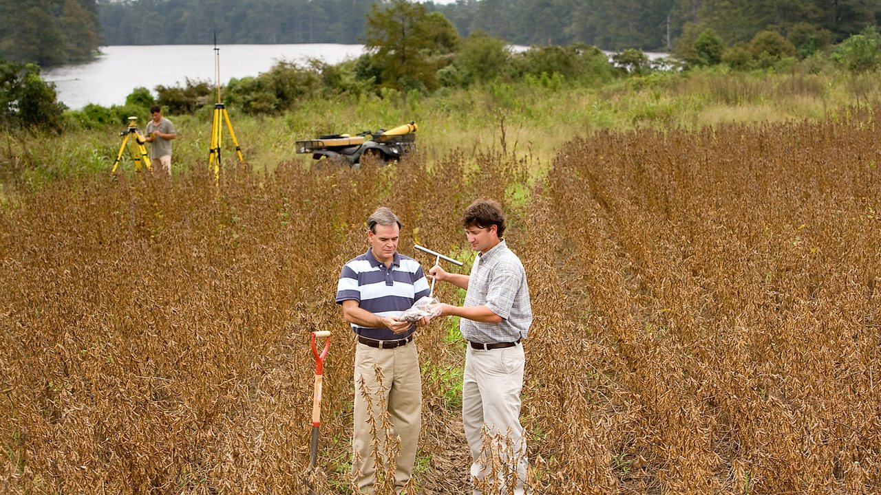 Two USDA-ARS researchers examine a soil sample in a row-crop field while GPS equipment records the sampling area