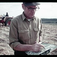 A conservation professional records notes on a soil map while standing in a no-till corn field.