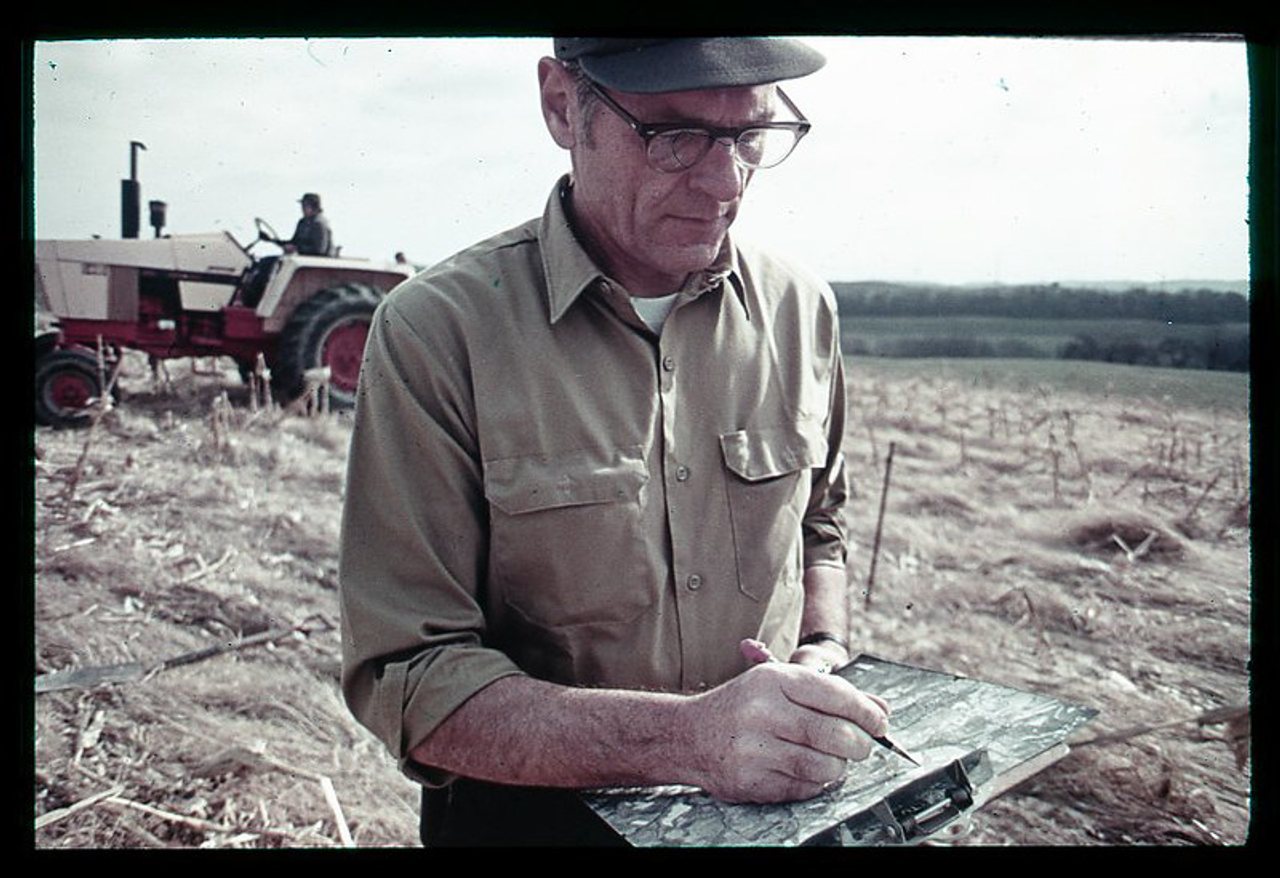 A conservation professional records notes on a soil map while standing in a no-till corn field.