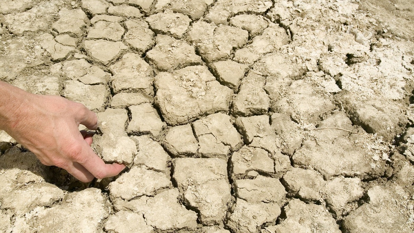 A hand touches cracked high-clay soil aggregates in a dry field surface.