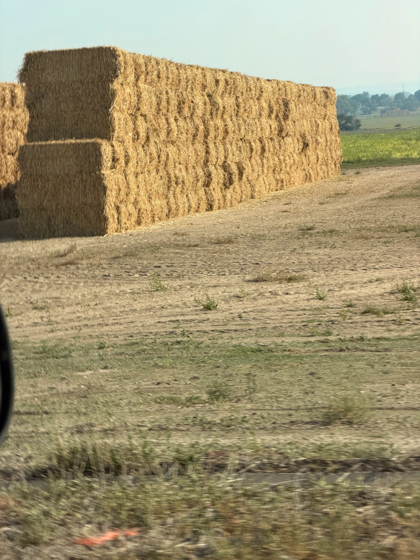 Rectangular hay bales stacked beside a dirt yard along the route.