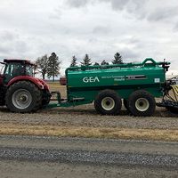 A tractor pulls a green manure applicator with hoses and soil-engaging equipment across a harvested field.