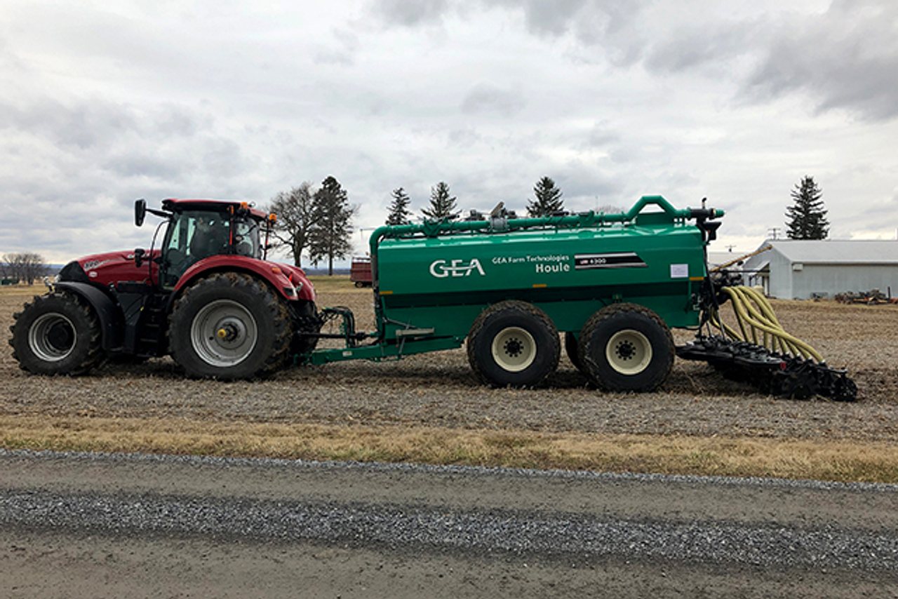 A tractor pulls a green manure applicator with hoses and soil-engaging equipment across a harvested field.