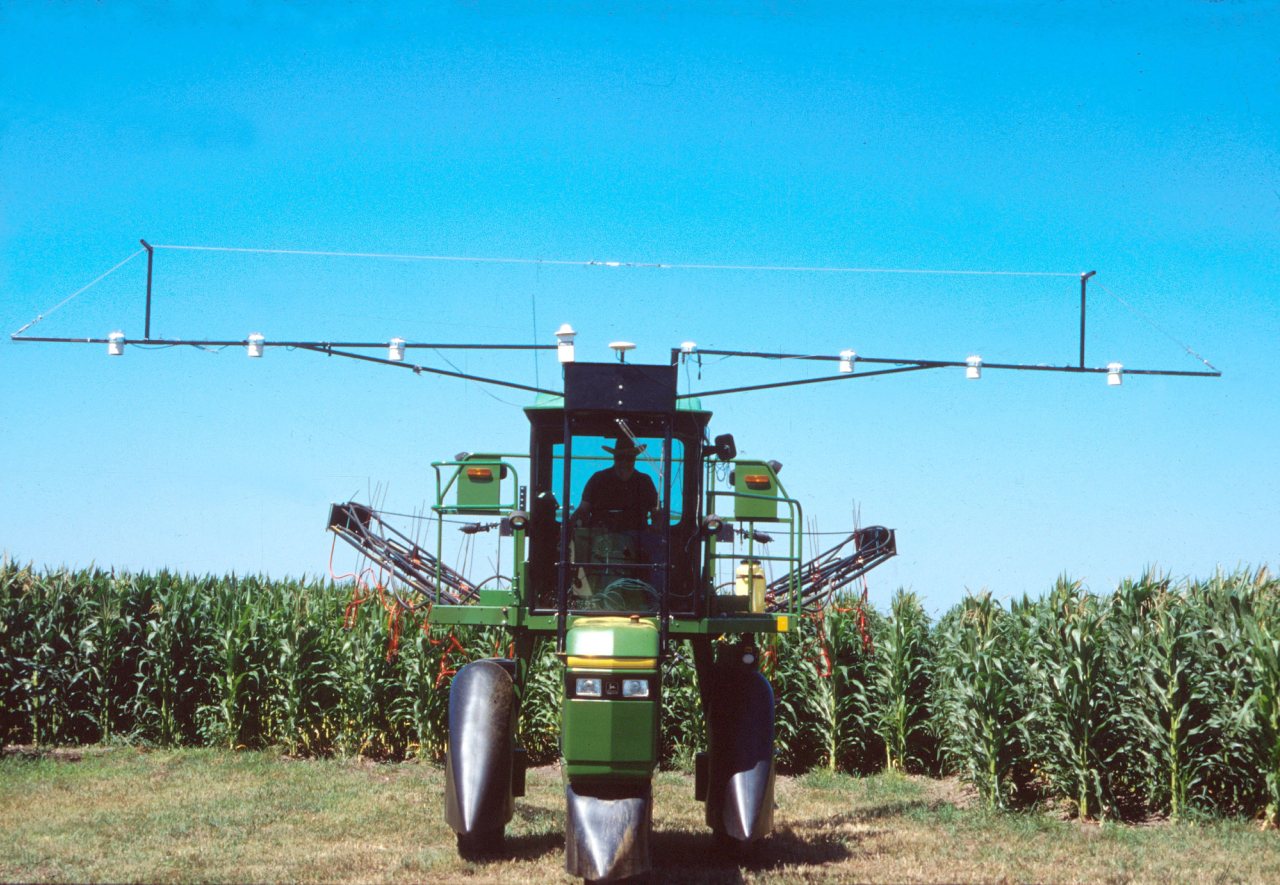 A high-clearance nitrogen applicator fitted with crop-canopy sensors stands in front of a green corn field.