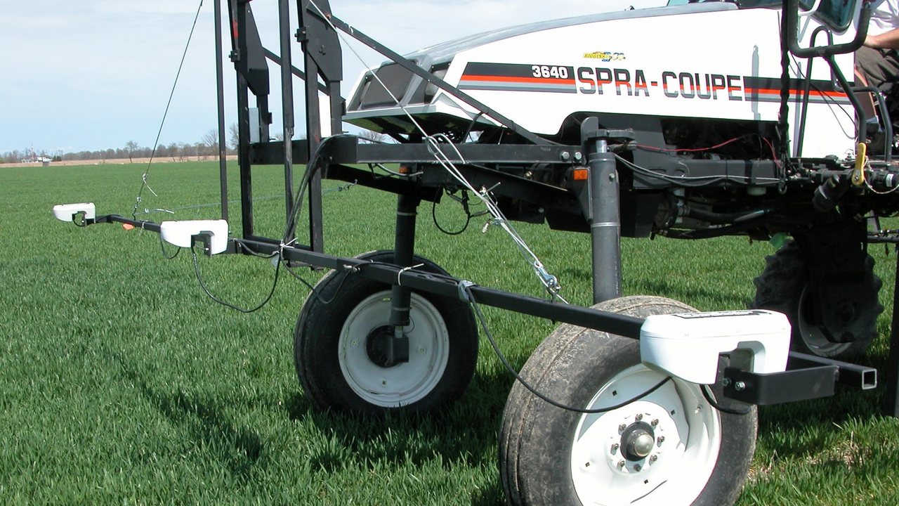 A field applicator fitted with light-reflectance sensors moves through a green crop field.