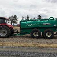 A tractor pulls a green manure applicator with hoses and soil-engaging equipment across a harvested field.