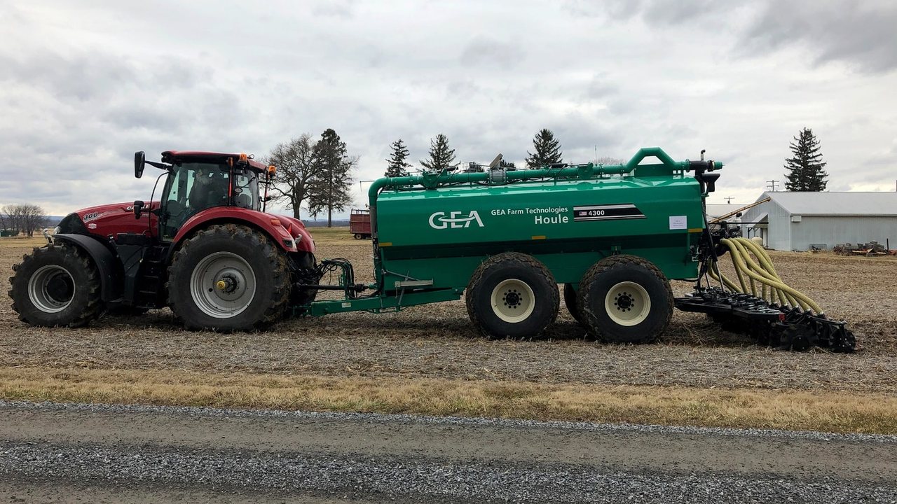 A tractor pulls a green manure applicator with hoses and soil-engaging equipment across a harvested field.