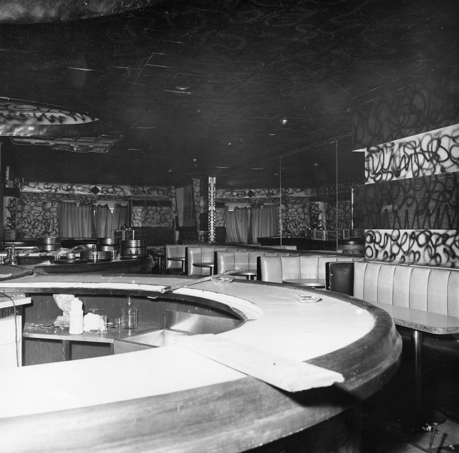 B&W photo of empty cafe: round bar in center with leather booth seating around