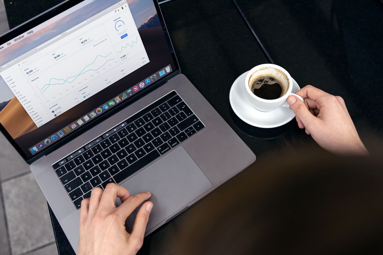 Un professionnel consulte des courbes de chiffres sur son ordinateur portable, une tasse de café à la main.