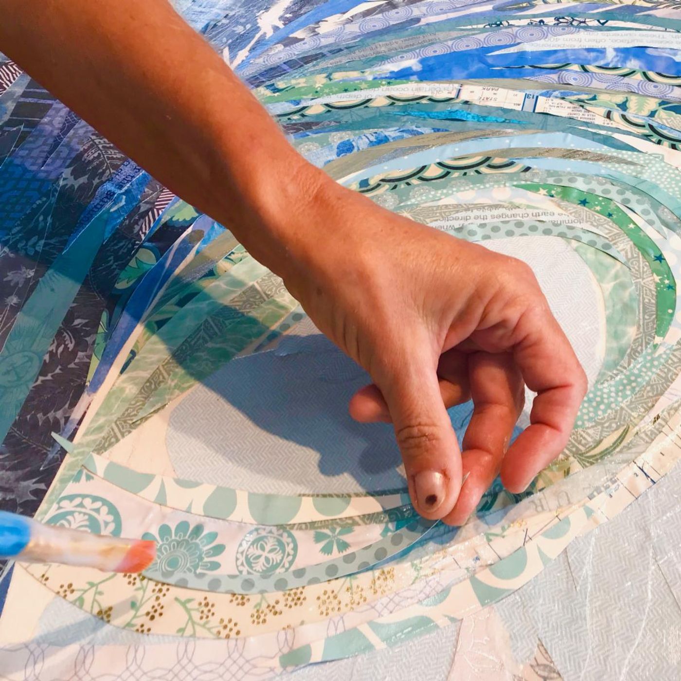 Jennifer's hand placing curved strips of patterned paper inside the spiraling curl of the Big Kahuna wave