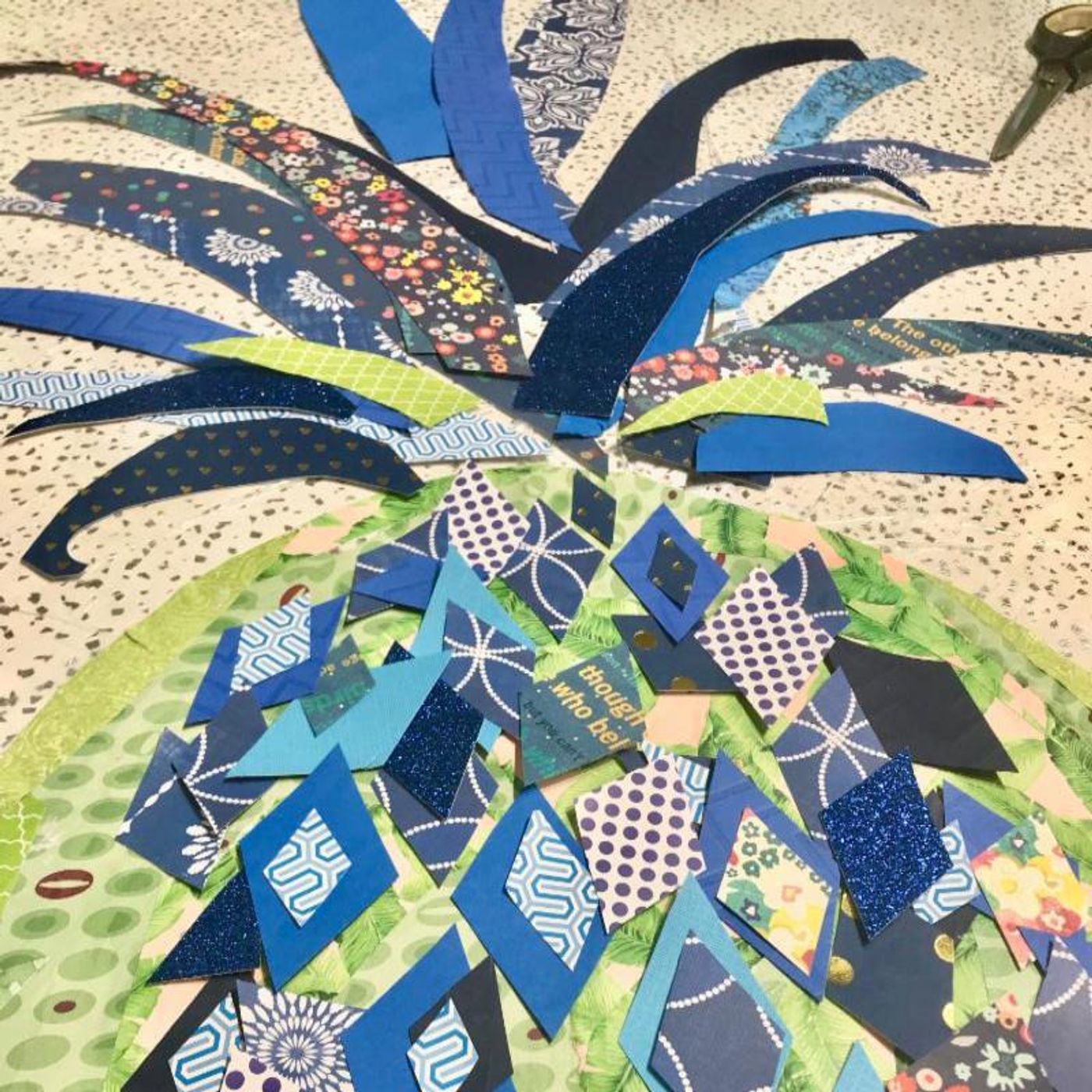 Close-up of a pineapple collage in progress — layered blue diamond-cut papers over a green paper body