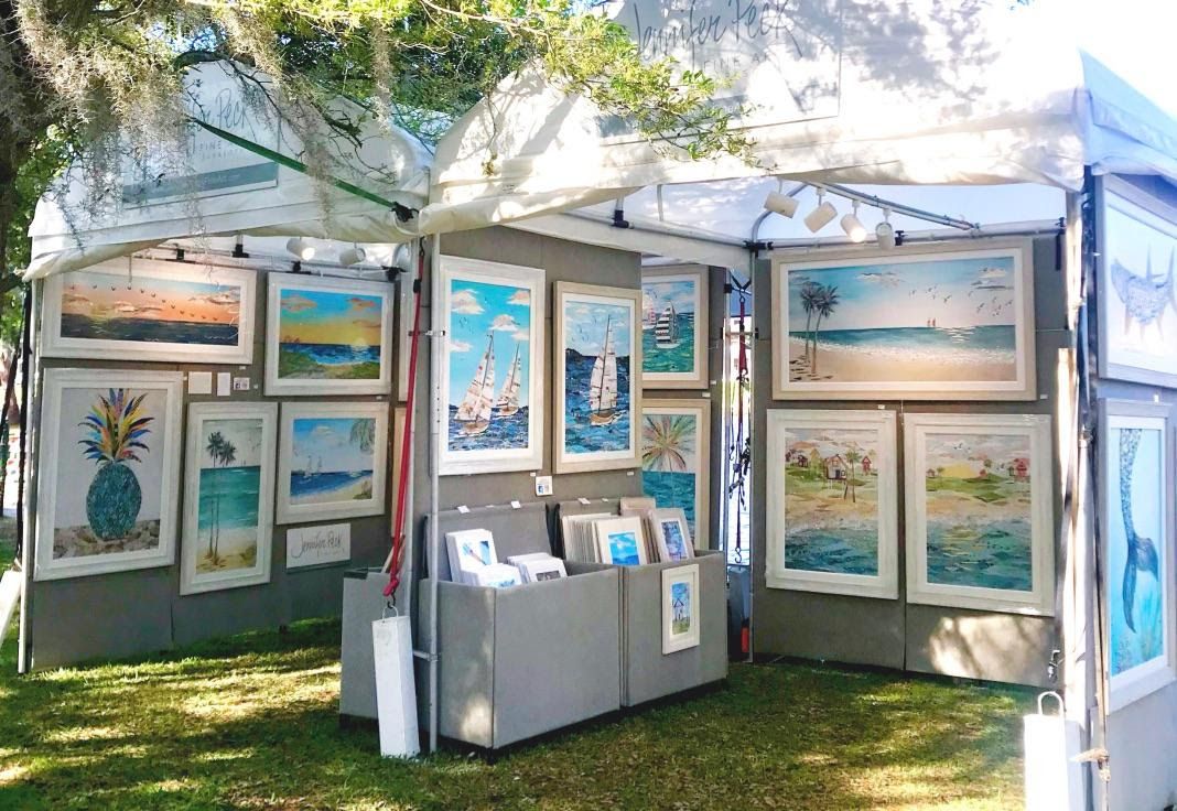 Jennifer's white festival tent hung with framed coastal collages — sailboats, beaches, a blue pineapple — print bins at the center.